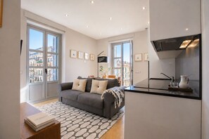 A modern living room with a grey sofa, a coffee table, and a kitchen area with a stove and sink.
