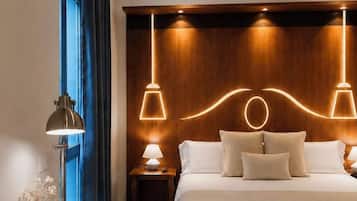 Una habitación de hotel con cama, lámparas de noche, un escritorio con silla y una ventana con cortinas.