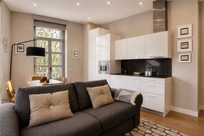 A modern living room with a sofa, a dining table, and a kitchen area with white cabinets and a black countertop.