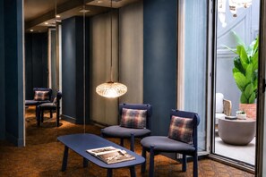 A modern lounge area with a bench, two chairs, a hanging light fixture, and a large window with a view of greenery. - Legazpi Doce Rooms & Suites (San Sebastián)