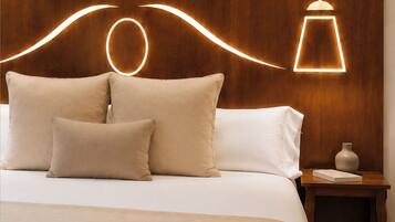 A neatly made bed with a wooden headboard, two pillows, a bedside table with a vase and book, and a modern pendant light.