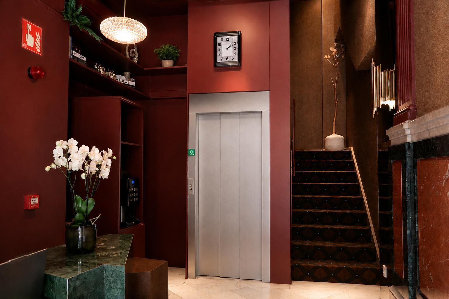 A hotel lobby with a reception desk, a clock, an elevator, and a staircase.