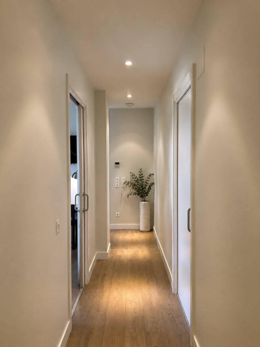 Un couloir étroit avec un plancher en bois et des murs blancs.