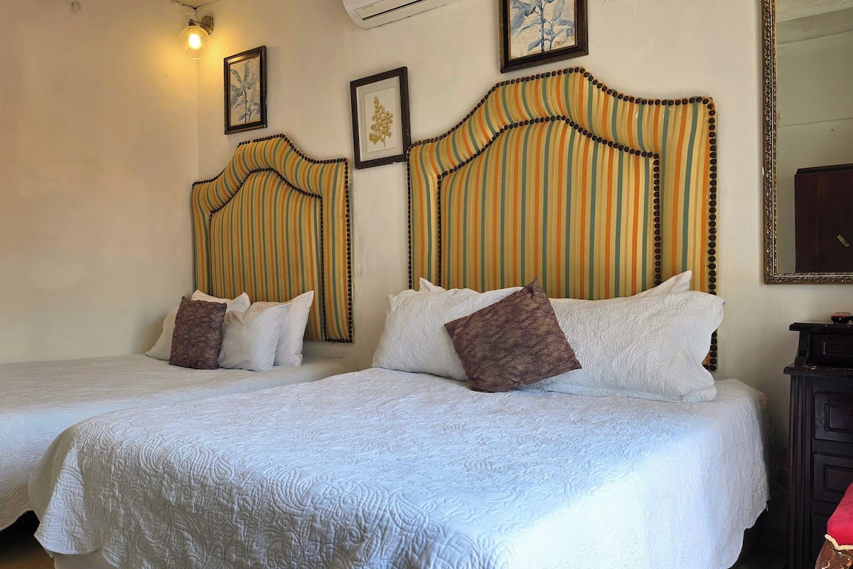 A hotel room with two beds, each with a white bedspread and pillows, a striped headboard, and framed artwork on the walls.