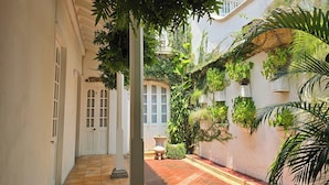 Un patio estrecho con suelo de baldosas, una puerta blanca con paneles de vidrio y una jardinera de piedra.