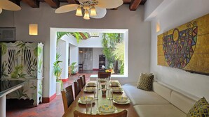 Comedor con una mesa larga dispuesta para una comida, rodeada de sillas, con vista a una cocina y comedor al fondo.