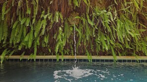 A swimming pool with a waterfall feature surrounded by dense ferns. - Hotel Casa la Tablada (Cartagena)