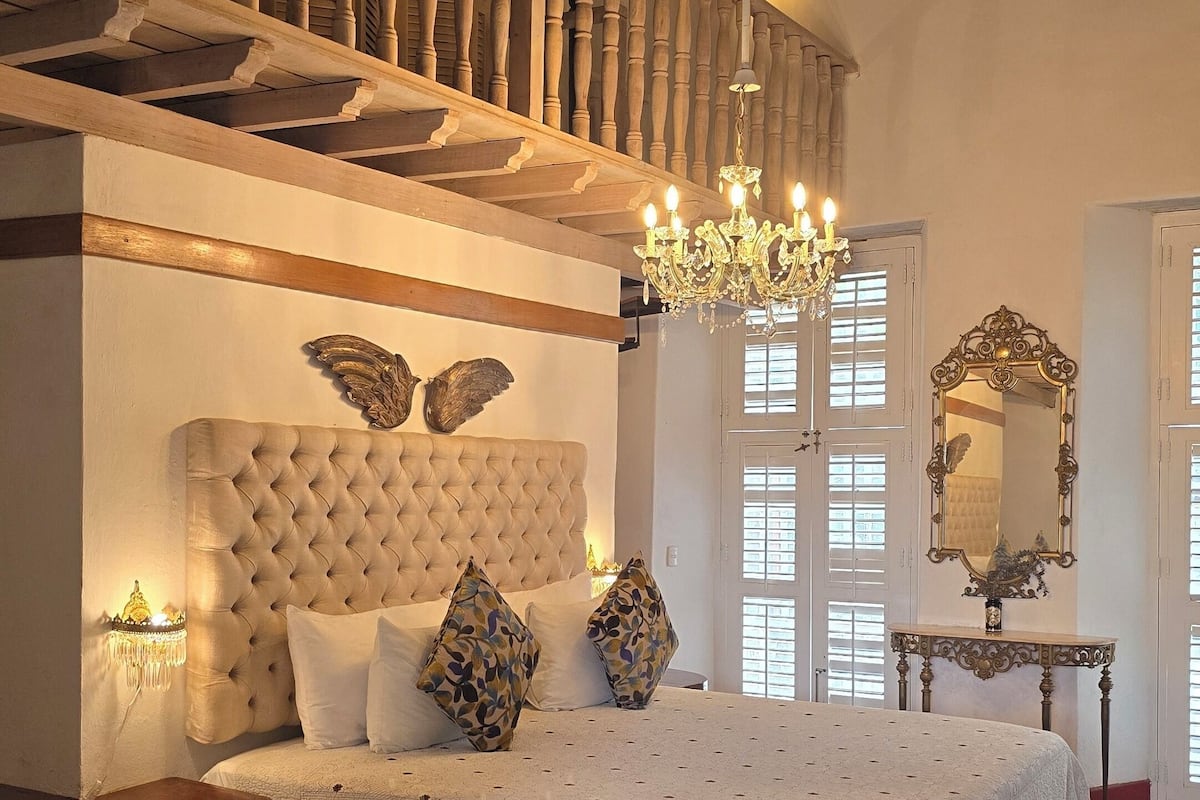 A bedroom with a large bed, a chandelier, a wooden ceiling, and a mirror.