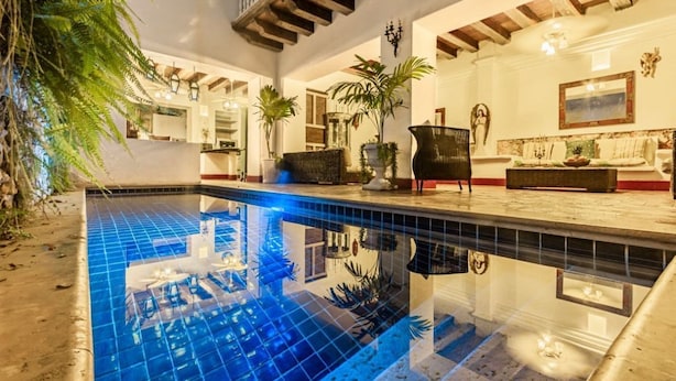 Un área de piscina con suelo de baldosas, techo de madera y un espacio de descanso con sofá y sillones.