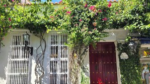 Un edificio con paredes blancas, una puerta roja y un balcón con plantas y flores.