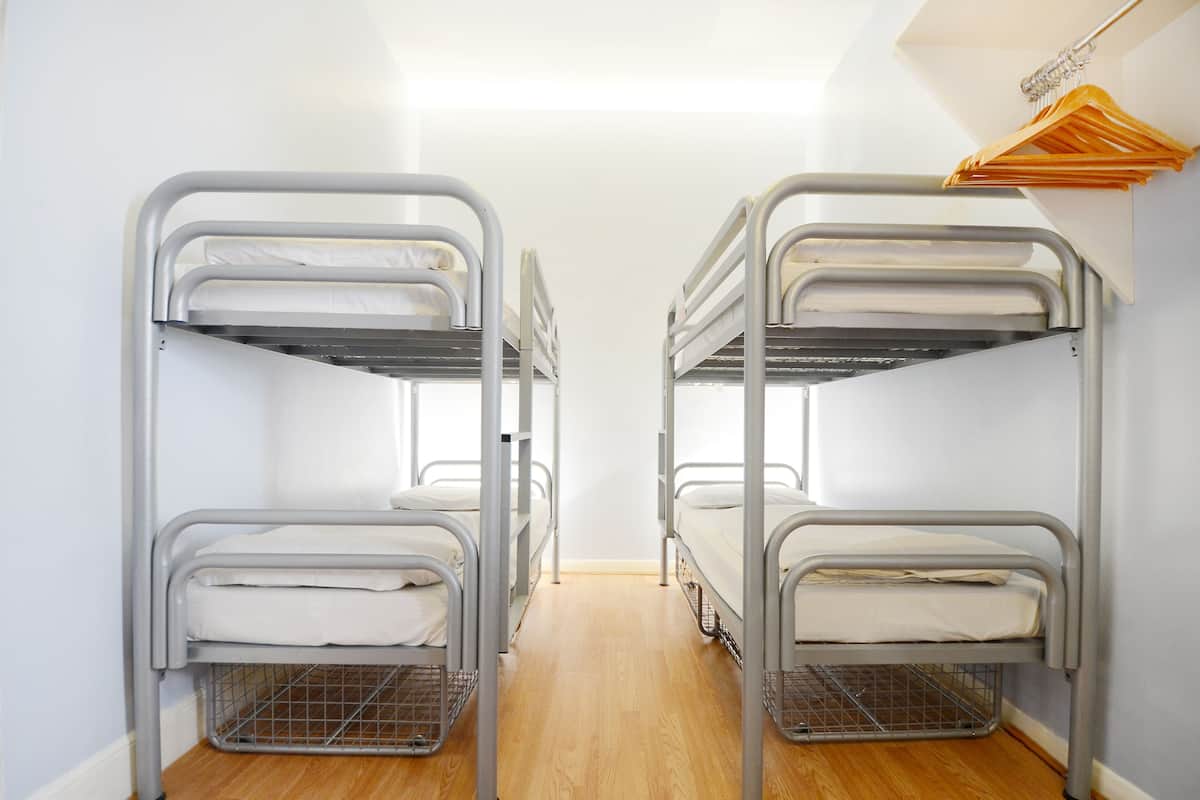 A room with two bunk beds, wooden flooring, and a closet with hanging clothes.