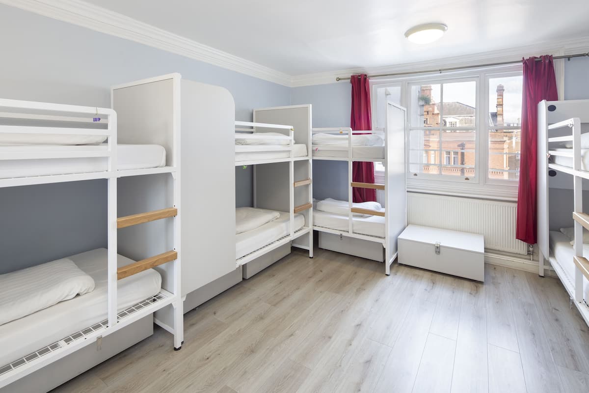 A room with bunk beds, a window with red curtains, and a radiator.