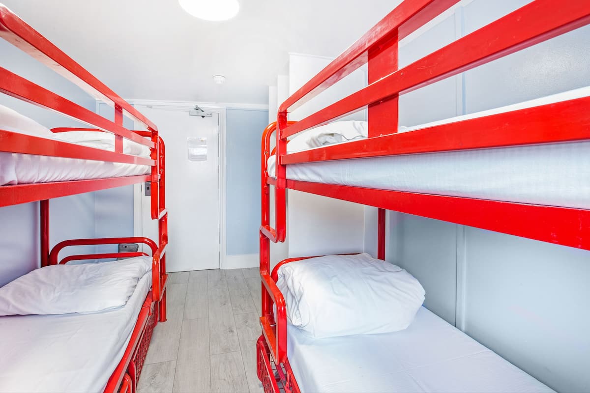 A room with two bunk beds, each with white bedding and red metal frames.