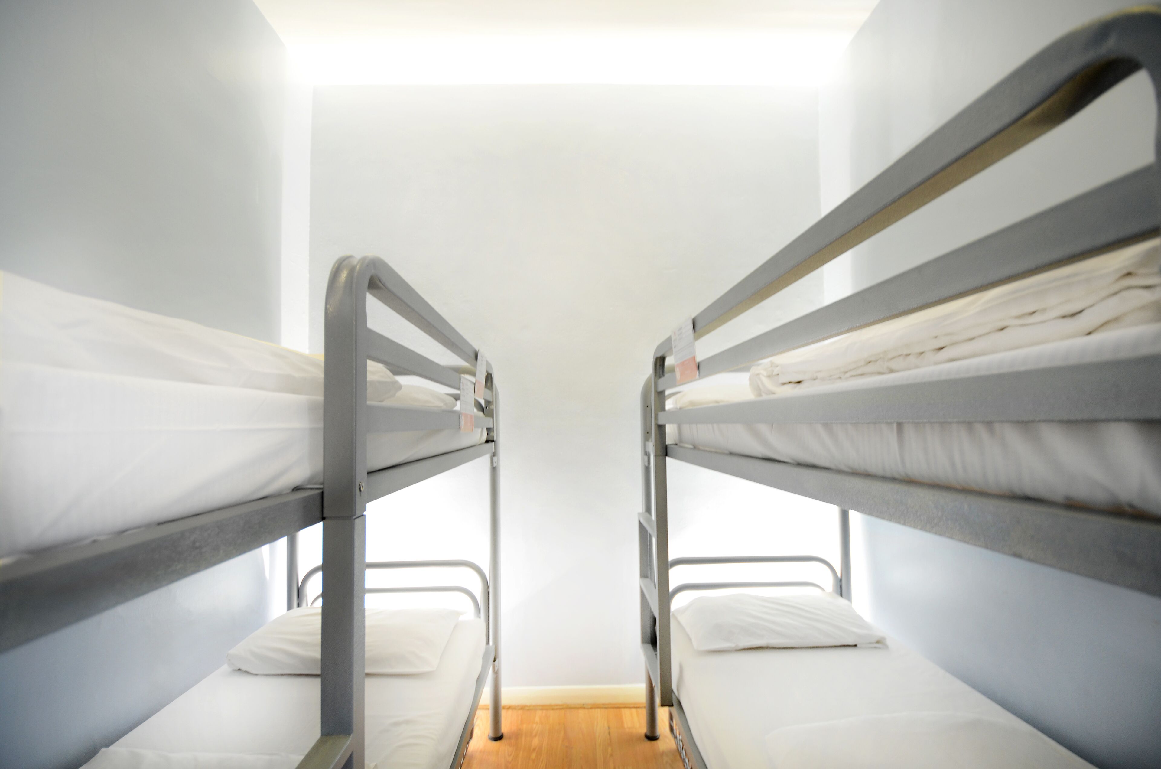 Une chambre avec un lit superposé, dotée de barrières métalliques et de linge de lit blanc.