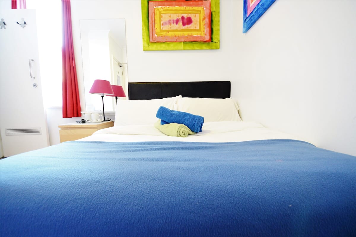 A neatly made bed with a blue blanket, a white pillow, and a rolled-up towel.