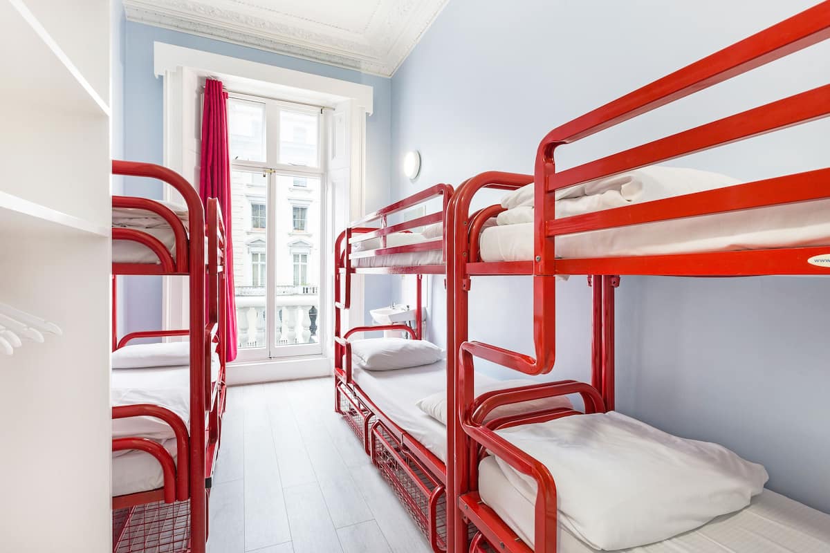 A room with bunk beds, a window with curtains, and a view of buildings outside.