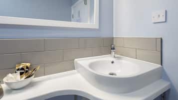 A bathroom with a white sink, beige tiles, and a mirror above it.
