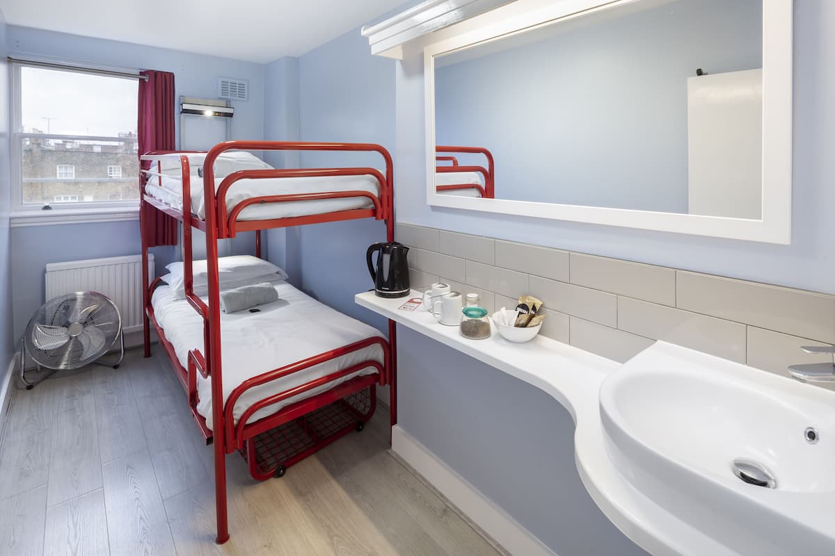 A bunk bed with a fan, a sink, and a mirror in a room with light blue walls and a window.