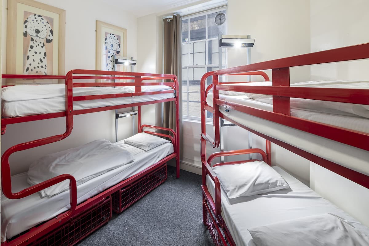 A dormitory room with bunk beds, a window with curtains, and framed artwork on the wall.