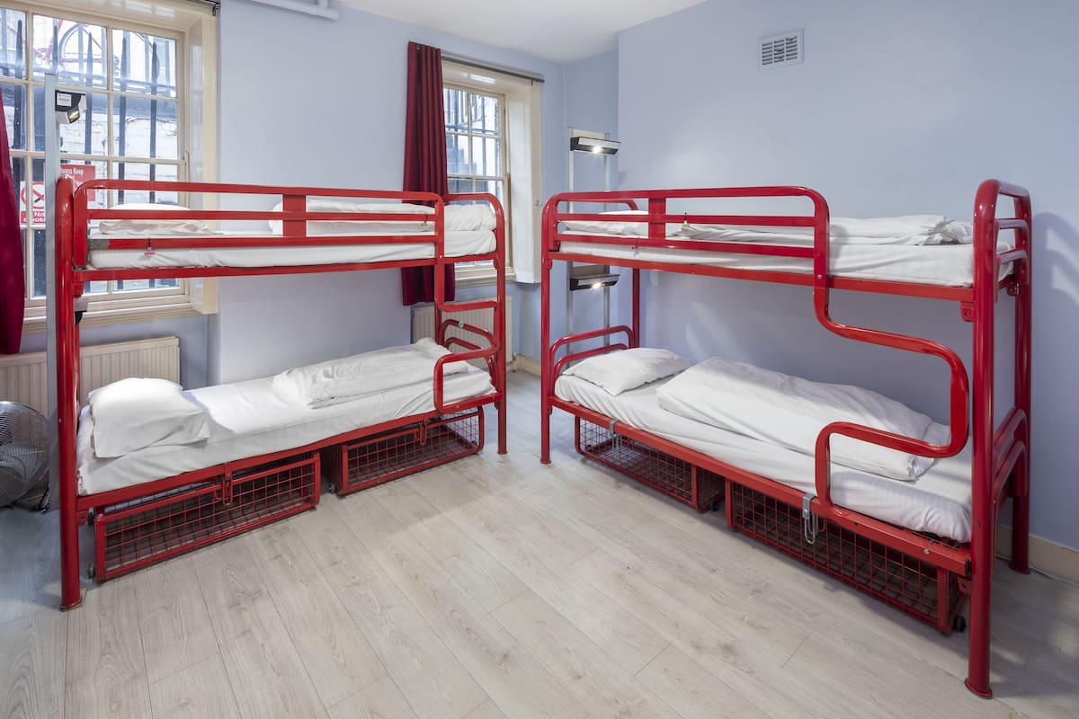 A room with two bunk beds, a window with curtains, a radiator, and a standing heater.