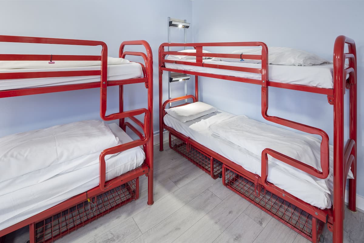 A room with three bunk beds, each with white bedding and red metal frames.