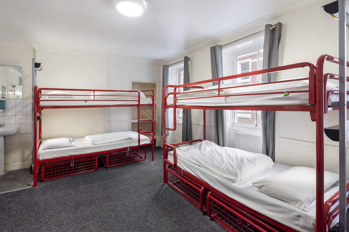 A dormitory room with bunk beds, a sink, and a window with curtains.