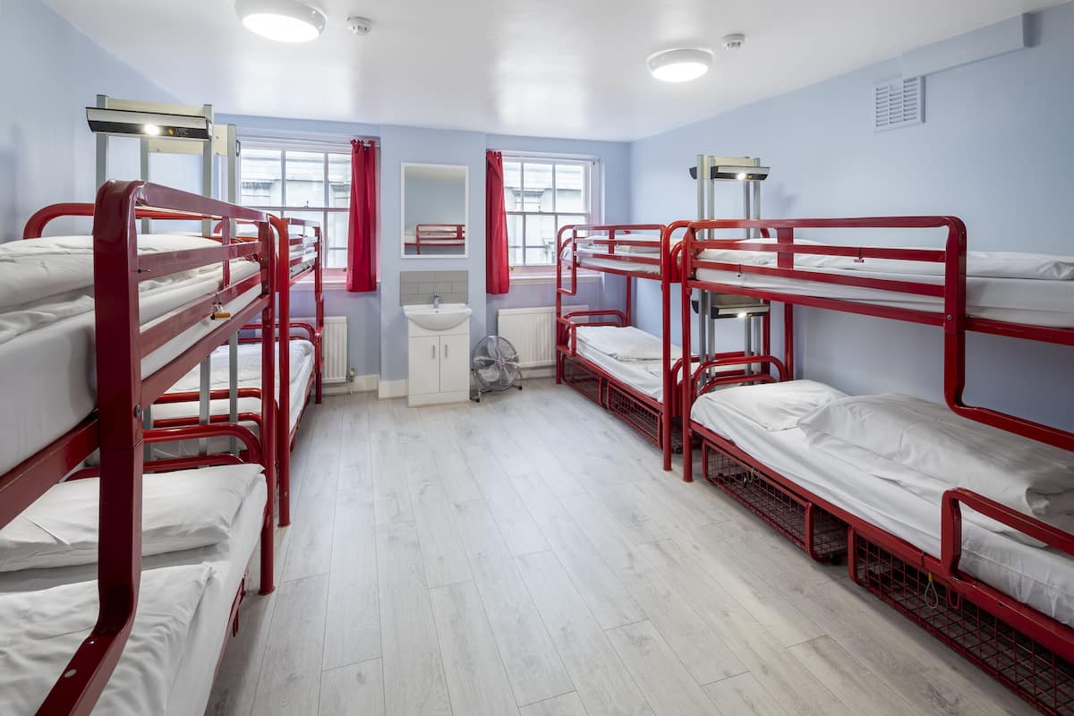 A dormitory room with bunk beds, a sink, and a window.