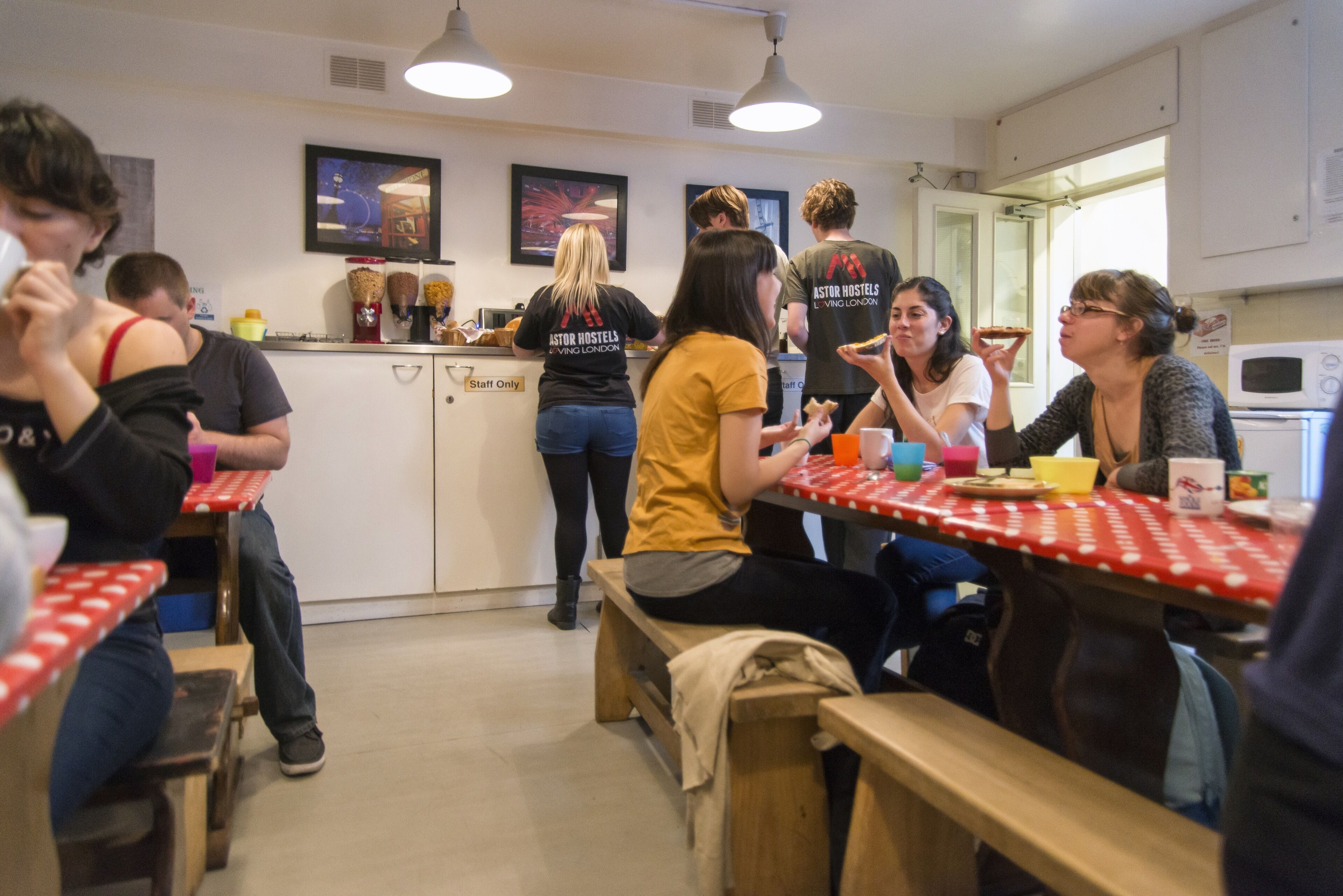 A communal dining area with tables and benches, a kitchen counter with various food items, and a sign indicating 'Staff Only'.