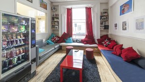 A modern living room with a sofa, a red table, and a vending machine. - Astor Kensington Hostel (London)