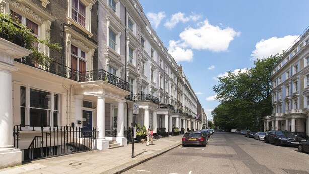 A row of classic, multi-story buildings with white facades and black railings. - Astor Kensington Hostel (London)