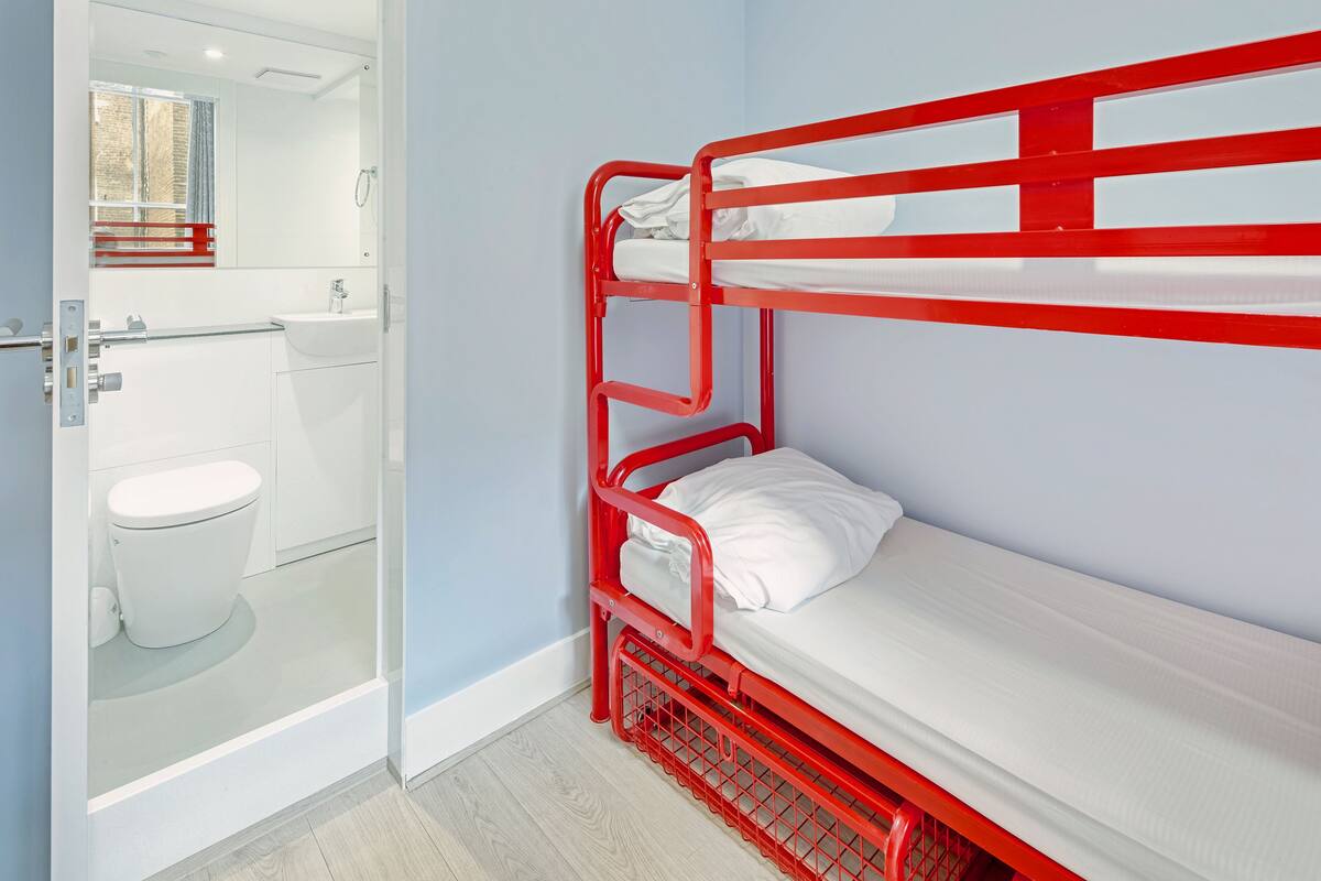 Ein Stockbett mit weißer Bettwäsche in einem Badezimmer mit Toilette und Waschbecken.