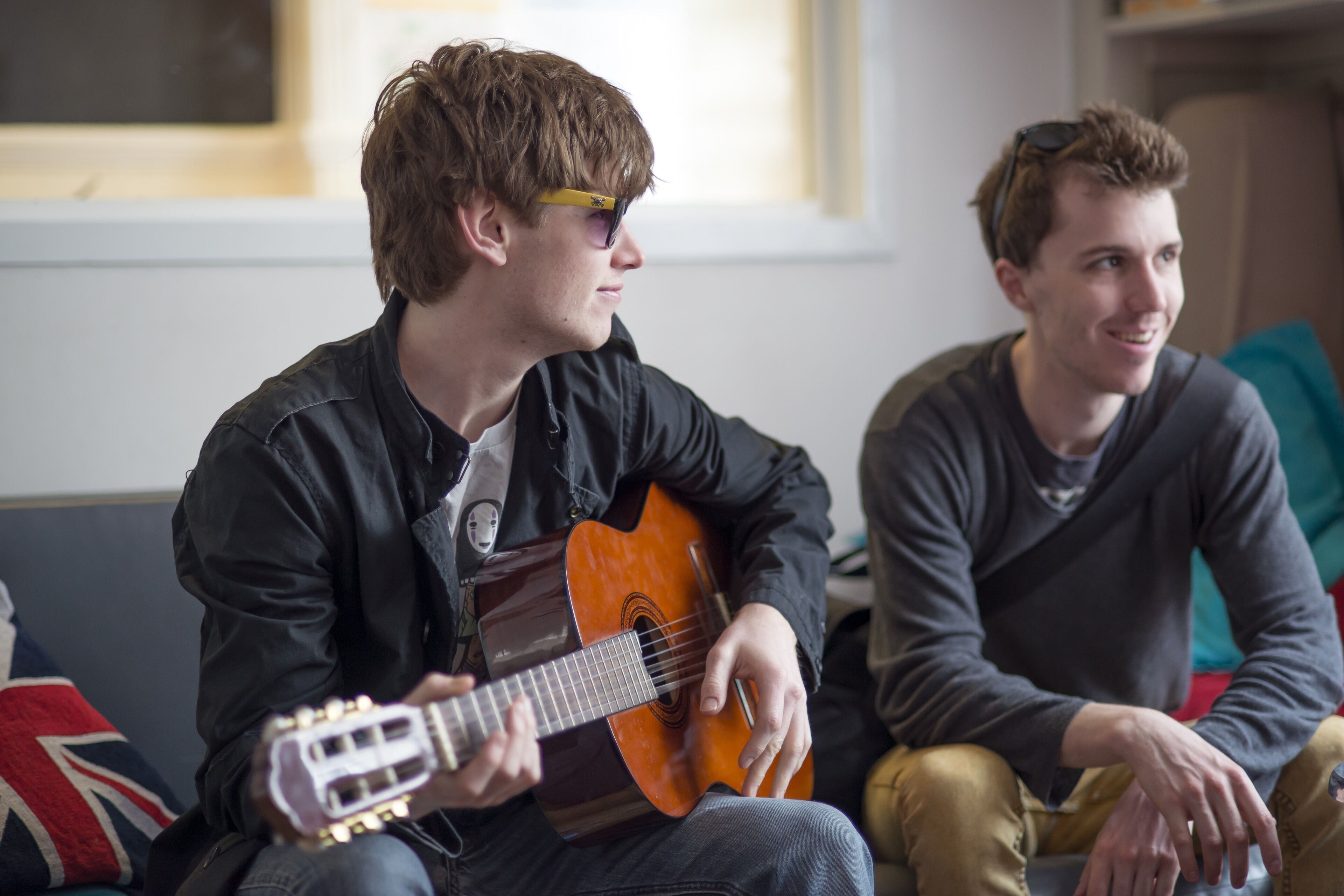 Two individuals seated on a couch, one playing an acoustic guitar.