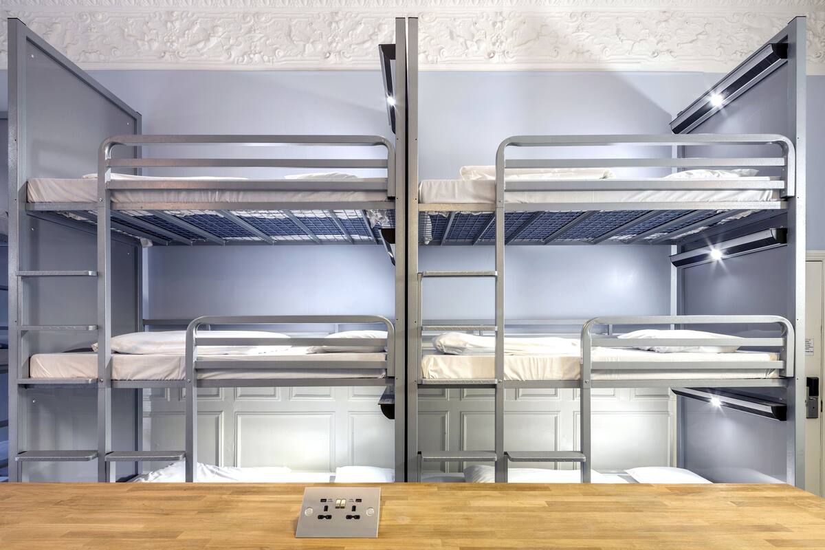 Ein Schlafraum mit Etagenbetten, im Vordergrund ein Holztisch und eine weiße Decke mit Zierleisten.