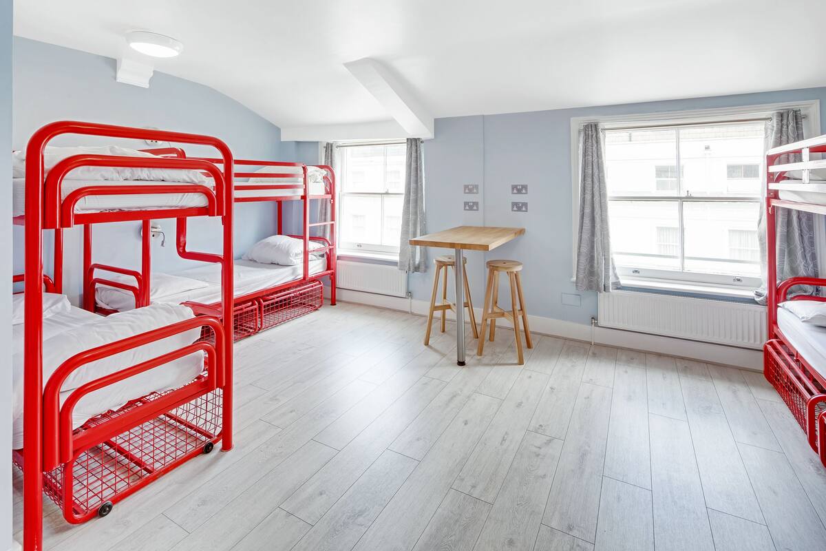 Ein Schlafsaalzimmer mit Etagenbetten, einem Holztisch und einem Fenster mit Vorhängen.