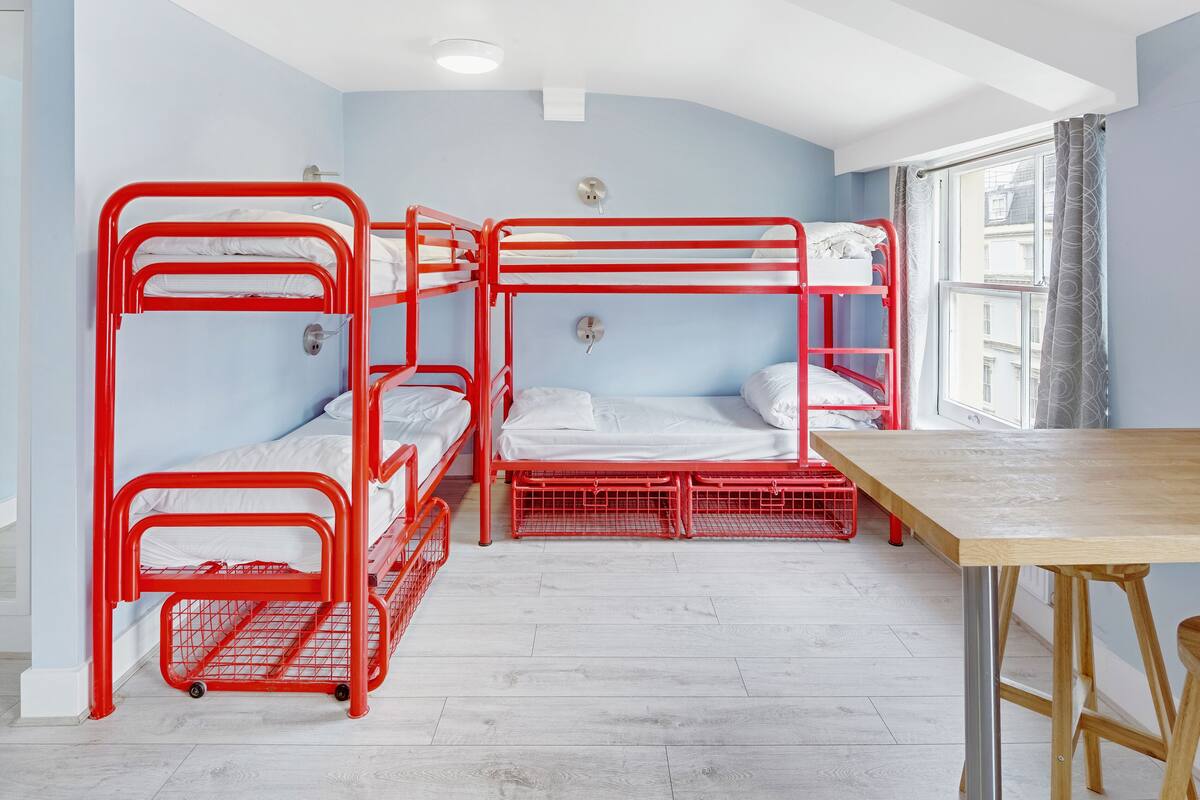 Ein Zimmer mit drei Etagenbetten, einem Holztisch und einem Fenster mit Vorhängen.