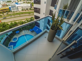 Un edificio moderno con balcón de vidrio que da a una piscina y vista a la calle.