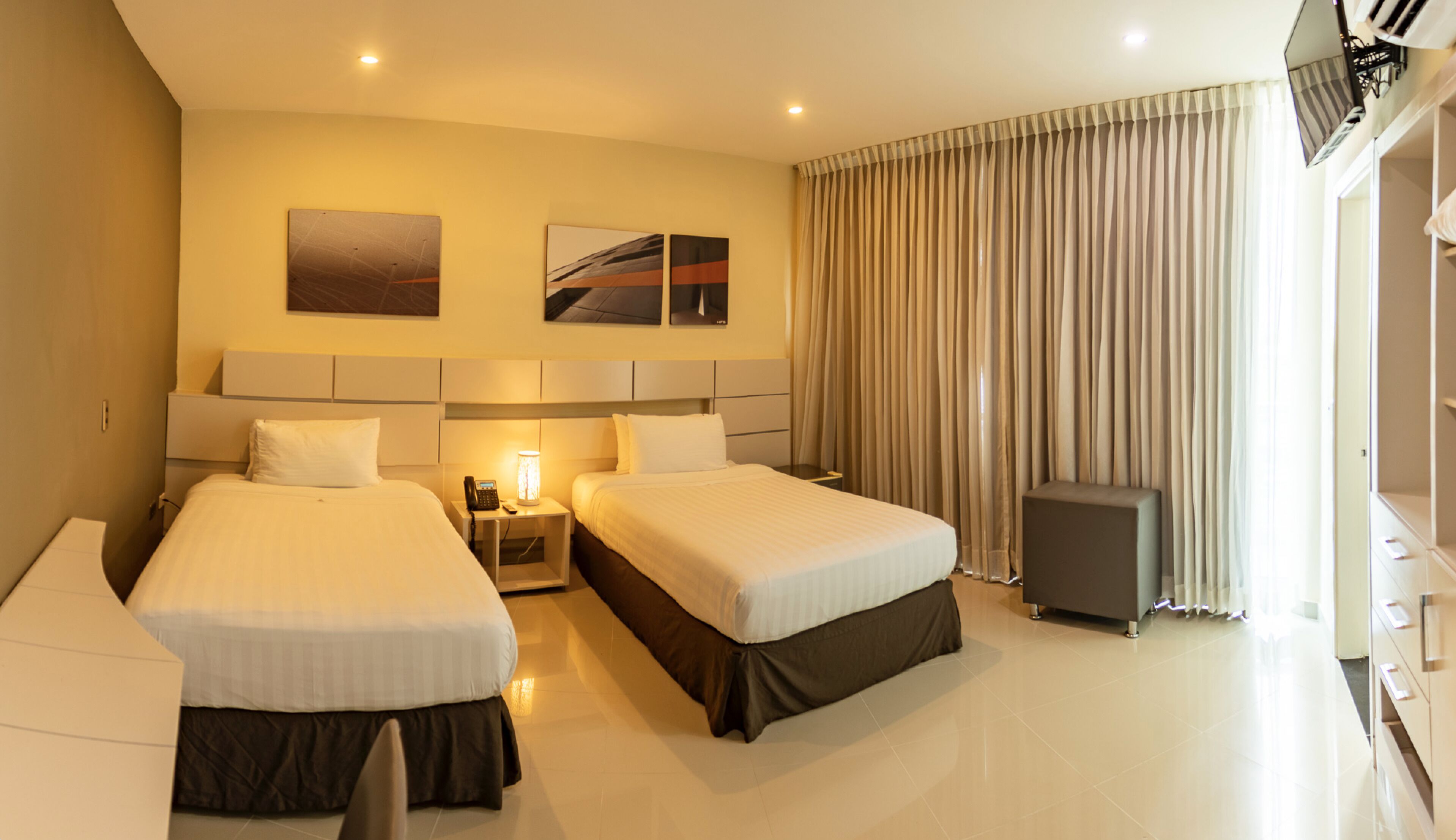 A hotel room with two beds, a desk, a lamp, a telephone, and a speaker.