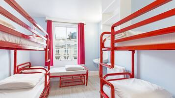 A dormitory room with bunk beds, a window with curtains, a radiator, and a sink.