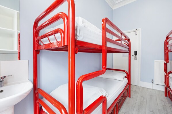 Une chambre avec des lits superposés, un lavabo blanc et une porte visible au fond.