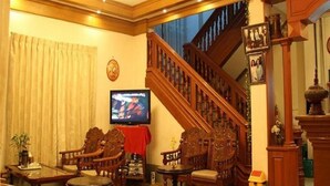 A traditional living room with a wooden staircase, a television, and classic furniture. - Mr. Charles Hotel (Hsipaw)