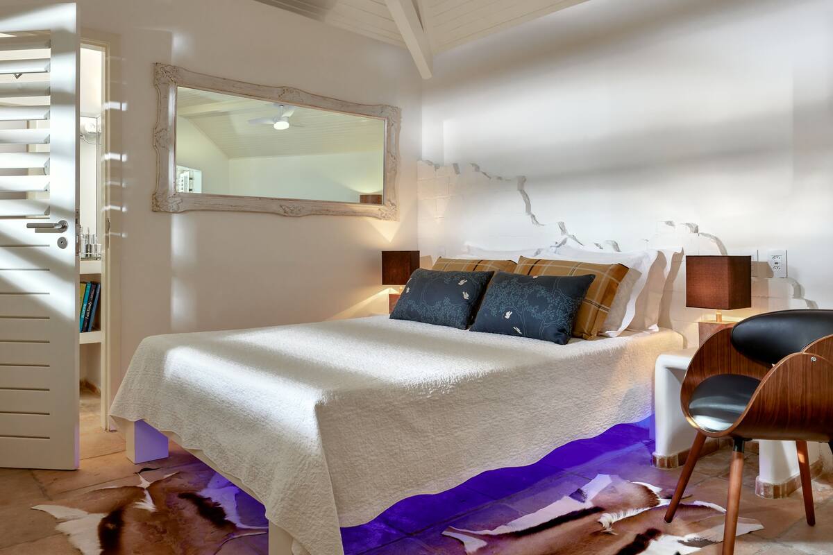Un dormitorio con cama, una silla, un espejo y una pared con un adorno.