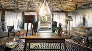 Habitación con techo de paja, una mesa de madera, sillas y vistas al exterior.