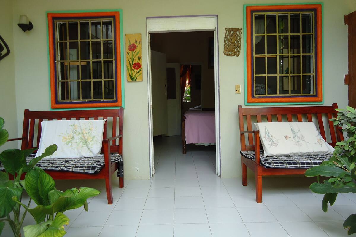 A room with two wooden benches, a bed, and a door leading to another room.