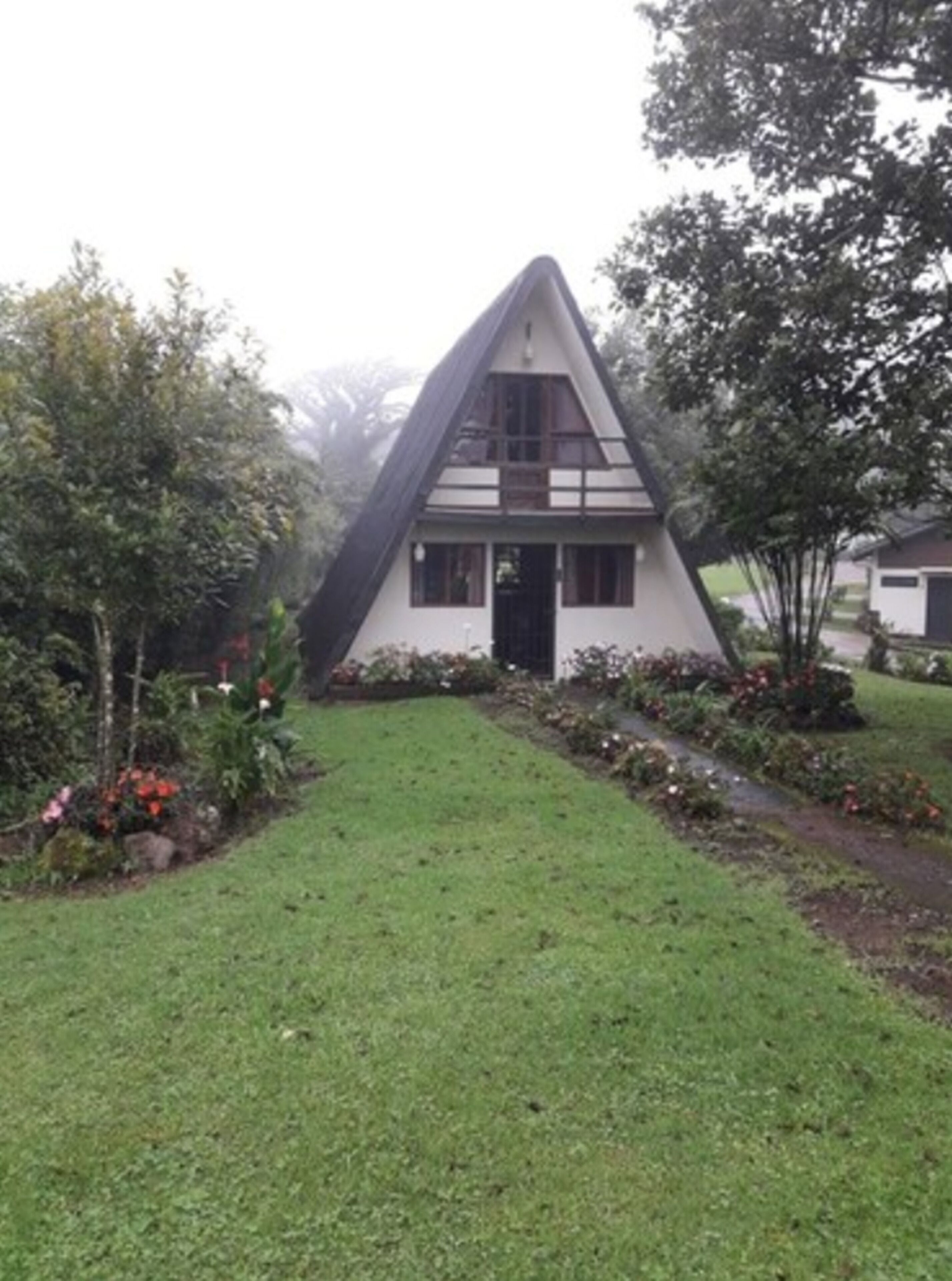 A triangular house with a central entrance, surrounded by a well-maintained lawn and flower beds.