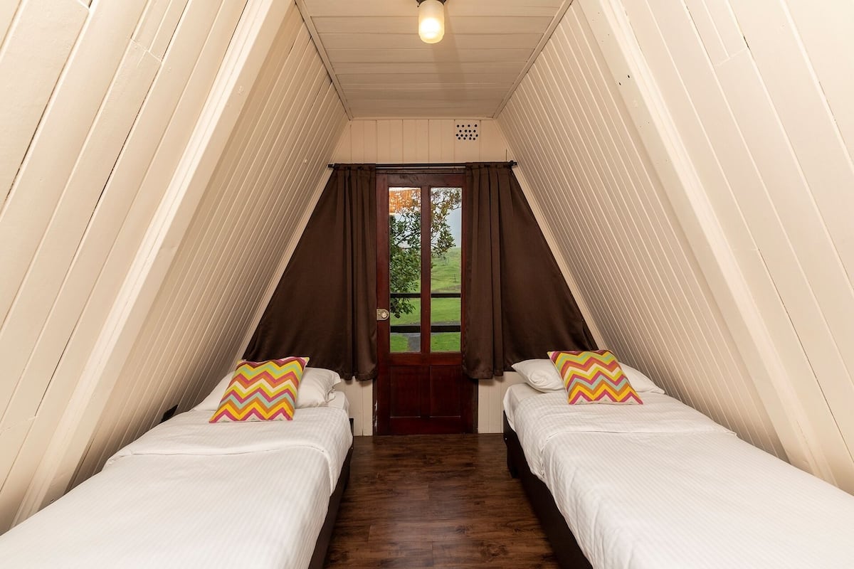 A narrow, sloped room with two beds, wooden flooring, and a door leading outside.