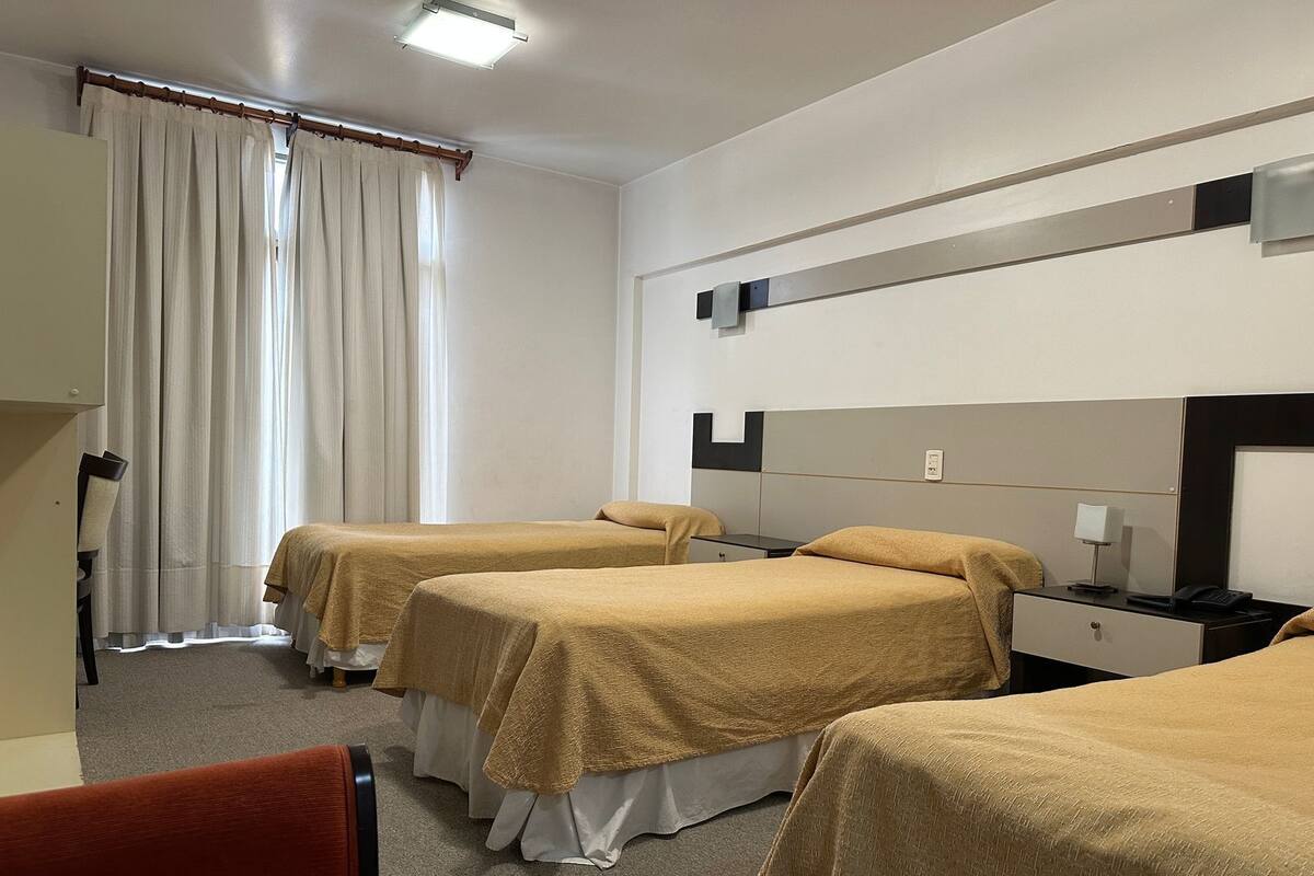 A hotel room with two beds, a desk, a chair, and a window with curtains.