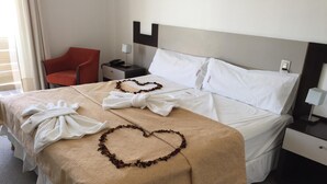 A hotel room with a bed, a nightstand, a red chair, and a window with curtains. - Hotel Nuevo Mundo (San Rafael)