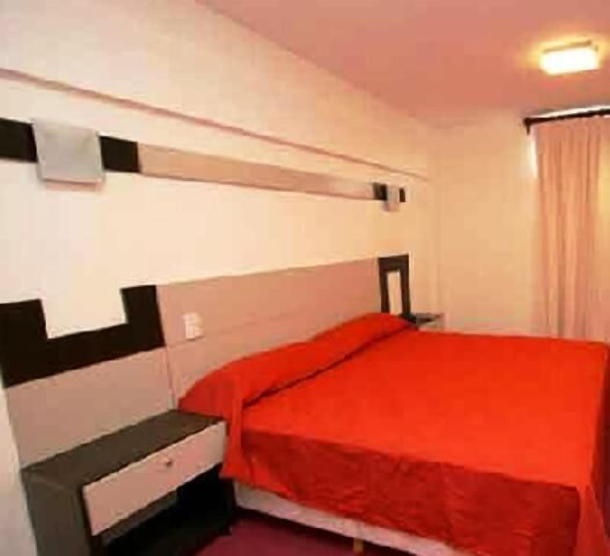 A single bed with a red bedspread in a room with a white and black headboard.