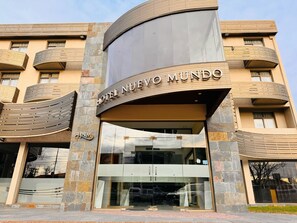Entrada de un hotel con fachada curva, grandes puertas de vidrio y un letrero que dice "HOTEL NUEVO MUNDO".