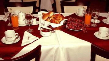 A breakfast setting with a table set for two, including croissants, grapes, and orange juice.